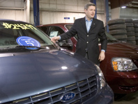 [Conservative Leader Stephen Harper stands between minivans after placing a sign on the windshield while visiting a car dealership in New Hamburg, Ontario] 8 January 2006
