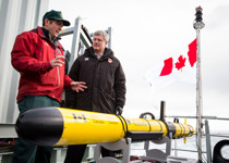 [Prime Minister Stephen Harper watches as Ryan Harris, Parks Canada, gives a scientific equipment demo aboard the HMCS Kingston as part of the 2014 Search for Franklin Expedition along the Northwest Passage] 24 August 2014