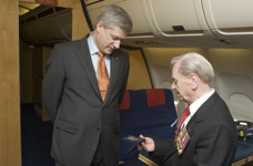[Second World War veteran Alex Hall shows one of his many service medals to Prime Minister Stephen Harper on the Airbus en route to Normandy, France to mark the 65th anniversary of D-Day] 5 June 2009
