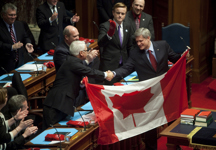 [Prime Minister Stephen Harper and British Columbia Premier Gordon Campbell wave a Canadian flag in the British Columbia Legislature in support of the Canadian athletes following the Prime Minister's address to the house in Victoria, British Columbia] 11 February 2010