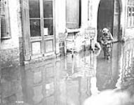 A Canadian Signaller repairing a wire in a street flooded by the enemy before he left Valenciennes. November, 1918 Nov. 1918.