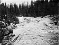 Indians running a boat through the Rapids on the Second Portage. The boats are run in the Channels of the River thereby avoiding the heavier swells in the main part of the River, which is a mile wide and almost impossible to run a boat through ca. 1900-1925