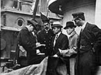H.H. Stevens (centre) interviewed by reporters, while Inspector Reid (centre Left) looks on, on board the "Komagata Maru" in English Bay, Vancouver, British Columbia 1914