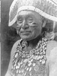 A Hupa Jumping dance costume, [California]. The ceremony was to avert pestilence. The head-dress was a wide band of deerskin with rows of red woodpecker crests and an edge of white deer hair sewn on it. A deer-skin robe was worn with shells 1924