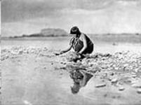 A housewife fills her jar with a gourd ladle at a shallow pond, San Ildefenso, Rio Grande River, [north New Mexico] 1926