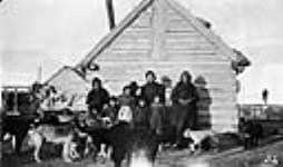 Métis family and dogs in front of a log house, Buffalo Narrows, Saskatchewan Early 1900s.