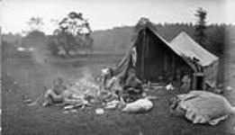 Gypsy woman, cooking in front of a tent, with her children at a camp near Lambton [Mills], Ontario, on the Humber River Oct. 12, 1918