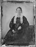 Massey Family: Unidentified woman wearing lace bonnet and dark silk gown, resting elbow on nearby side table ca. 1850s