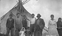 [Cree men, women, and children next to a teepee] Original title: Group of Indians and their summer home July 1927.