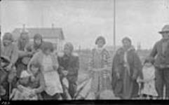 [Indigenous women and children (likely Gwich'in or Inuvialuit) at Aklavik, surrounding Ruth, who is reading a letter sent by Slim Richards from Paris, France] Original title: Natives at Aklavik - Ruth reading a letter from Slim Richards, Paris, France 1929