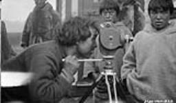 Unidentified Inuit man looking through a movie camera eyepiece [Assaajuq using a movie camera. Directly behind the camera is Usuutaapik. Qinnguq (Lai's father) is standing to the far right.] 1929