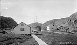 The wrecked "Canadian Raider" in cove at Port Burwell showing H.B. Co. Buildings in foreground August 1928.