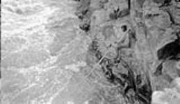 Kumaiak spearing fish from ledge at Bloody Fall June 1931.