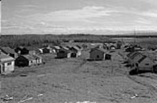[Large group of Gwich'in cabins with new police barrack in distant centre] Original title: Large group of Indian cabins new police barracks in distant centre 1945