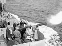 Unidentified personnel firing a two-pounder anti-aircraft gun aboard H.M.C.S. ASSINIBOINE, which is escorting a troop convoy from Halifax to Britain, 10 July 1940 July 10, 1940.