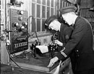 An unidentified Lieutenant watching an Electrical Artificer working on electrical equipment in the Electrical Artificers' Workshop, H.M.C. Dockyard, Halifax, Nova Scotia, Canada, 18 November 1942 November 18, 1942.