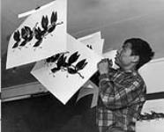 [Inuit artist (Iyola Kingwatsiak) in the craft centre at Cape Dorset, N.W.T., hanging prints to dry.] [1959]