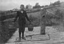 Unidentified boy carrying water buckets on yoke Aug. 1898