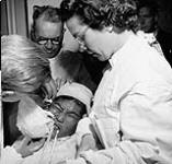 [Aboard C.G.S. "C.D. Howe" on Eastern Arctic patrol, Dr. C.E. Davies removes plaster mask (for fitting eye glasses) from Inuit girl, with Dr. R.S. Robertson (rear), and Nurse Isabel Thomas, C.N.I.B., July 1951] [ca. July 1951].