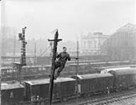 Signalman J. Bennett of the 1st Canadian Railway Telegraph Company, Royal Canadian Engineers (R.C.E.), installing wire on a pole in the railway yards, Louvain, Belgium, 6 January 1945 January 6, 1945.