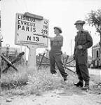 Sapper A.K. Jensen and Lance-Corporal D. Johnston, both of the Royal Canadian Engineers (R.C.E.), examining a sign indicating the distance to Paris, Vaucelles, France, ca. 18-20 July 1944 [ca. July 18-20, 1944].