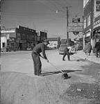 Deux employés municipaux (?) balayant de la terre accumulée sur la chaussée de la rue commerciale 1949