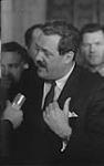 Le Président du Conseil privé, l'hon. Guy Favreau, est interrogé par des journalistes à la sortie de la Chambre des Communes après la clôture du débat et le vote sur le nouveau drapeau canadien décembre 1965