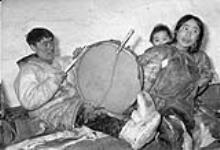 Ahkpa [Aggark] plays the drum while mother [Albina Aggark] and child [Ikitaq] look on 1949-50.