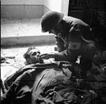 Private B.D. Flynn of the Regimental Aid Party, The Seaforth Highlanders of Canada, giving a drink of water to a badly-wounded German prisoner inside a church, Catona, Italy, 21 December 1943 Deember 21, 1943.