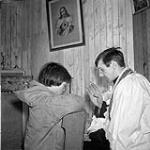 Kelora, a young Inuit boy, during confession to Father Joseph Choque at Oblate Fathers' Mission, Baker Lake (Qamanittuaq), Northwest Territories [Nunavut] March 1946.