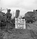 Corporal Urban Mayo of the 13th Field Company, Royal Canadian Engineers (R.C.E.), reading a sign which states, "You are entering Germany - Be on your guard", Wyler, Germany, 9 February 1945 February 9, 1945.