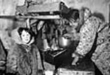 [Marion Bolt (left) and Annie Atatahak (right) working on a "kudlik", a lamp used for cooking and light.] 1949-1950
