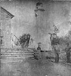 Light tower and partial view of surrounding buildings. Three unidentified people in foreground 1890