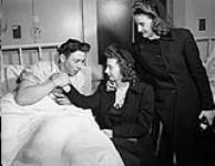 Unidentified survivor of the minesweeper H.M.C.S. ESQUIMALT, which was torpedoed by the German submarine U-190 on 16 April 1945, receives visitors at the Royal Canadian Naval Hospital, Halifax, Nova Scotia, Canada, April 1945 April 1945.