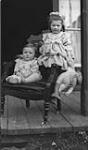 Two unidentified young children on verandah; written on front of doll "I Use Comfort Soap It's All Right" ca. 1907