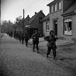 Soldiers of the Lincoln and Welland Regiment walking through the streets chasing German paratroopers out of town 11 Apr. 1945