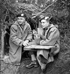 Captain D.N. McDonald, 12th Manitoba Dragoons, and Major R.B. MacNeill, The Queen's Own Cameron Highlanders of Canada, working outside a dugout in the Hochwald, Germany, ca. 10-11 March 1945 [ca. March 10-11, 1945].