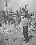 War correspondant James Cassidy standing in front of still burning ruins 17 Aug. 1944