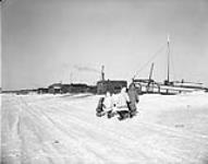 Two Inuit women and two children walking towards a boat, Aklavik, Northwest Territories March 1956.