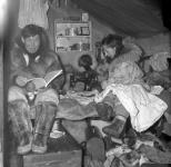[Inuk man reading a translation of the Book of Wisdom with an Inuk woman sewing]. Original Title: The Eskimos enjoy reading the new translation of the Book of Wisdom 1950