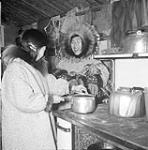 [Two women have a conversation while preparing a meal on a stove] Original title: Eskimo women using kitchen Whiteman's equipment. 1950.
