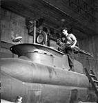 Sergeant A.H. Calder of the Canadian Army Film and Photo Unit, who carries a camera and tripod, examining one of the German miniature two-man submarines discovered in a shipyard at Kiel, Germany, 18 May 1945 May 18, 1945.