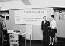 Leader of the New Democratic Party, Mr. T.C. Douglas, standing beside a sign erected by the ND Youth, reading "The Tommy Douglas Mouseland--The tale of the black cats and the white cats--On a long playing recording" 196-