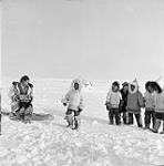 Inuit woman Martha plays the concertina for a group of dancing boys, Resolute Bay (Qausuittuq), Nunavut [The woman has been identified as Edith Patsauq] March 1956.