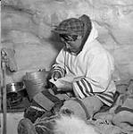 Inuit carver Etcolopea at work in his igloo putting the finishing touches on a seal carving with a file