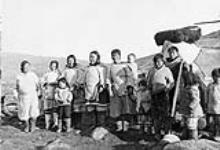 A group of people standing beside a topak. [Left to right: Ittuqquaq, Martha Kanayuk, Towkie, Joe Akpalialuk (boy in front) Aulaqiaq, Aluki Akpalialuk and unidentified baby, Miali Battye holding Aluki's hand, Kanayuk Ishulutak(late husband of Elisapee Ishulutak) Nuqinngaq (standing behind Kanayuk) and unidentified child.] [1934]