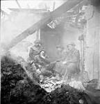 Infantrymen of the Regina Rifle Regiment keeping warm in the smoldering ruins of a house, Zyfflich, Germany, 9 February 1945 February 9, 1945