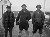 Three men standing in a row behind the Hudson's Bay Company building [Nutaraluk (left), unidentified man (centre) and Thomas Siatalaaq (right)] 1944.