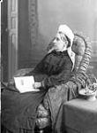 Mrs. J.B. Monk in a chair with a book on her lap Oct. 1886