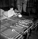 War correspondent Shelley Mydans of Life magazine typing an article while sitting beside a display of swords surrendered by Japanese officers, Japan, August 1945 August 1945.